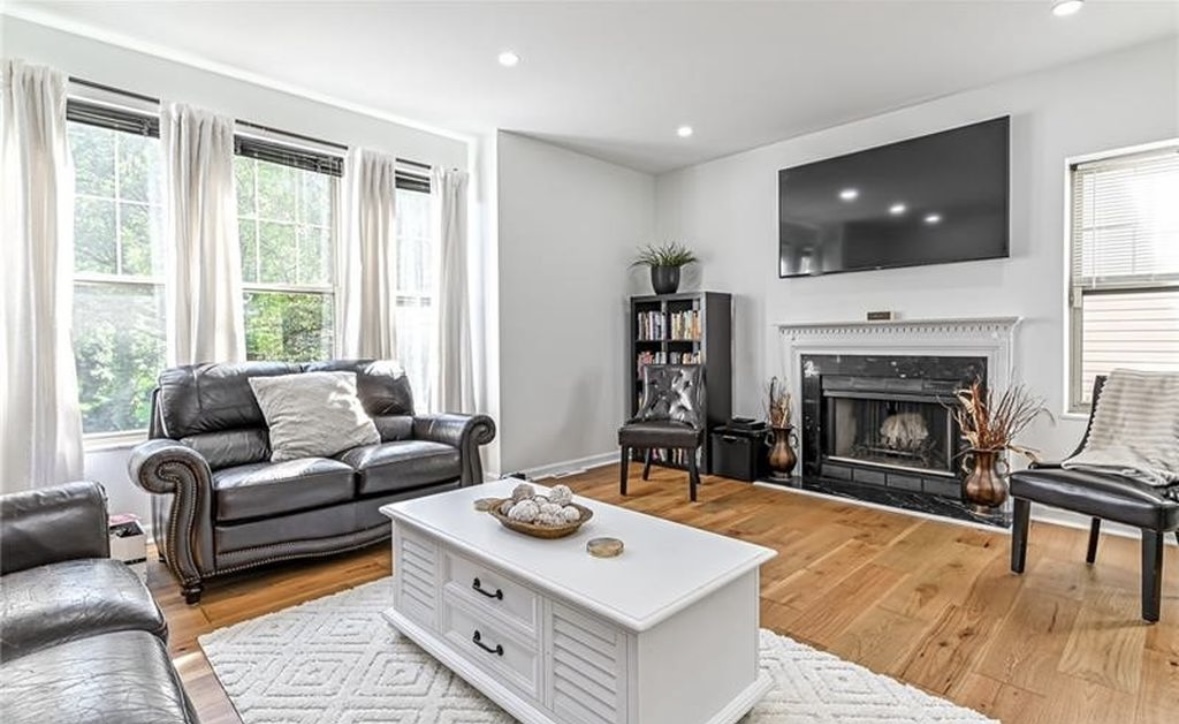 After: the living room refreshed with light walls, wood floors, leather seating, and a white coffee table